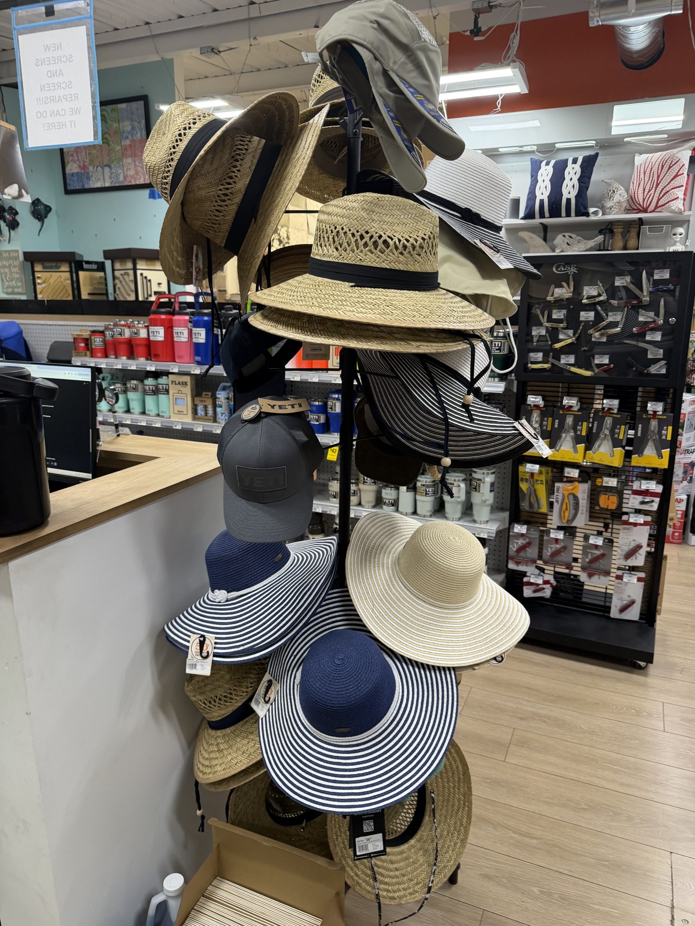 Display rack filled with wide-brim straw hats, striped sun hats, and YETI baseball caps near YETI drinkware at Hessler Paint & Hardware in Delray Beach, Florida.
