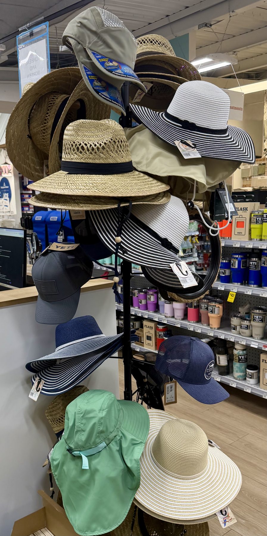 Display rack filled with wide-brim sun hats, straw hats, neck-flap UV protection hats, and YETI caps near YETI drinkware at Hessler Paint & Hardware in Delray Beach, Florida.